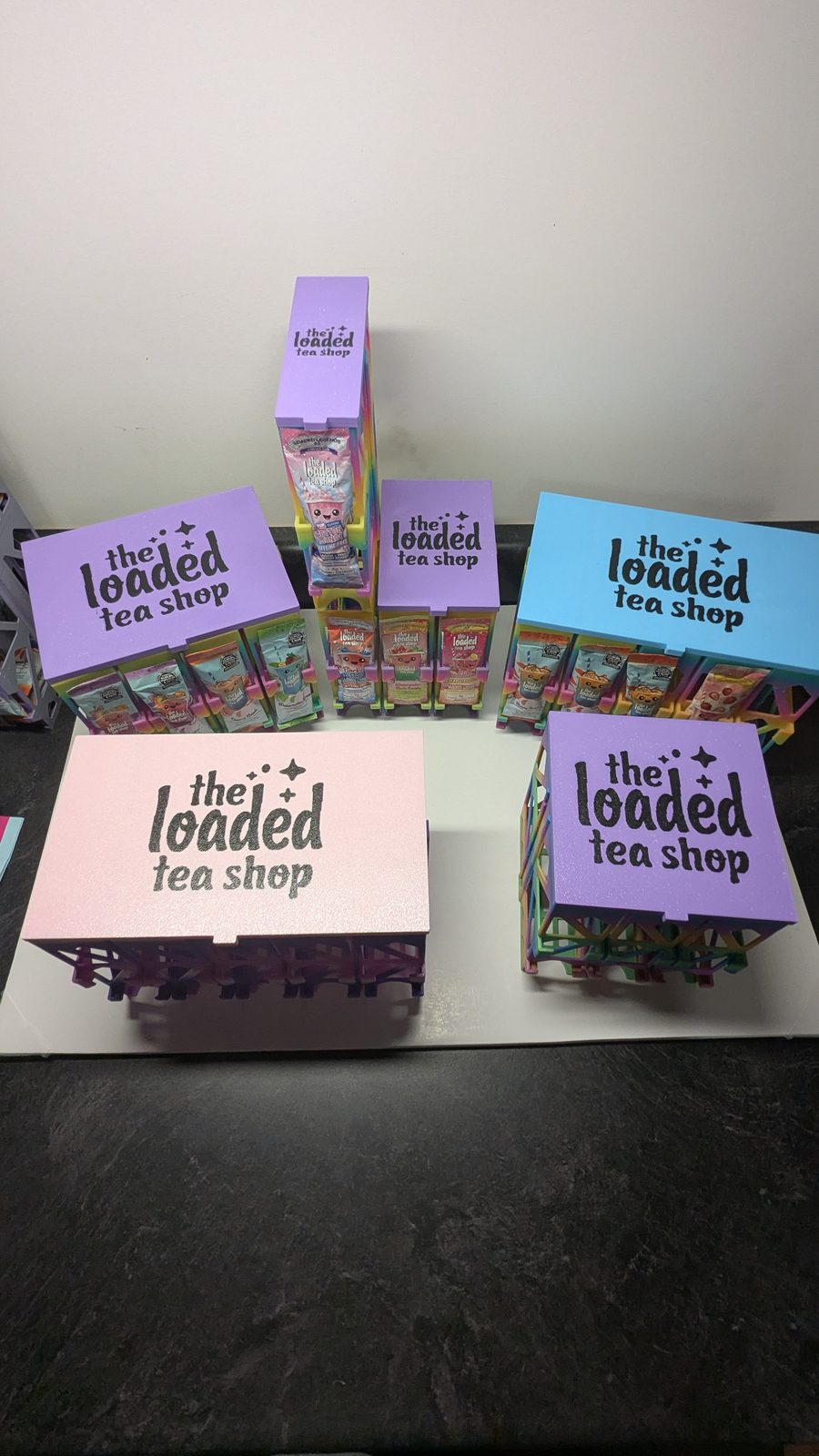 Loaded tea holders topped with pink, purple and light blue logo lids, with tea packets visible